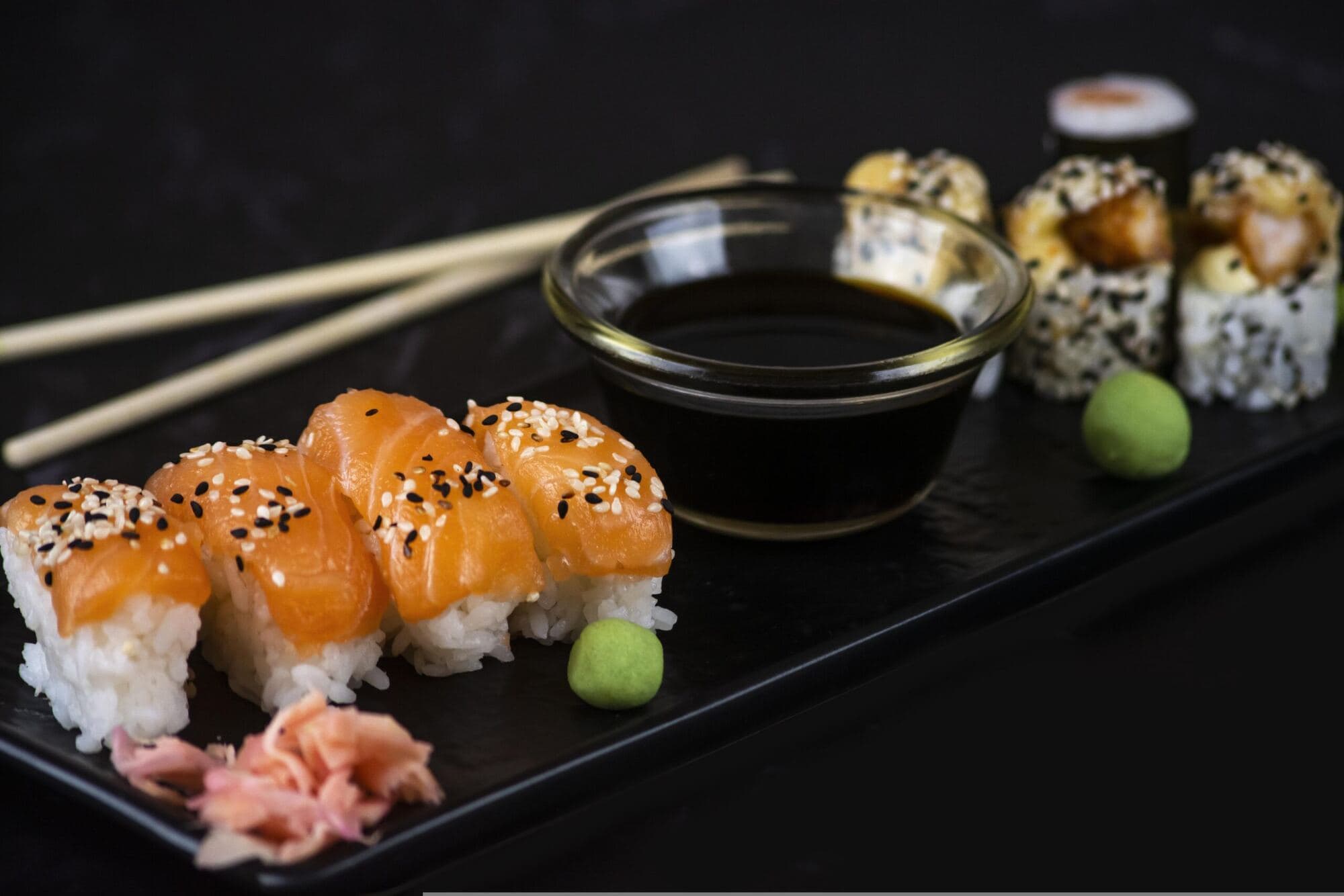 Laxsushi med sesam, soja och wasabi på ett svart fat